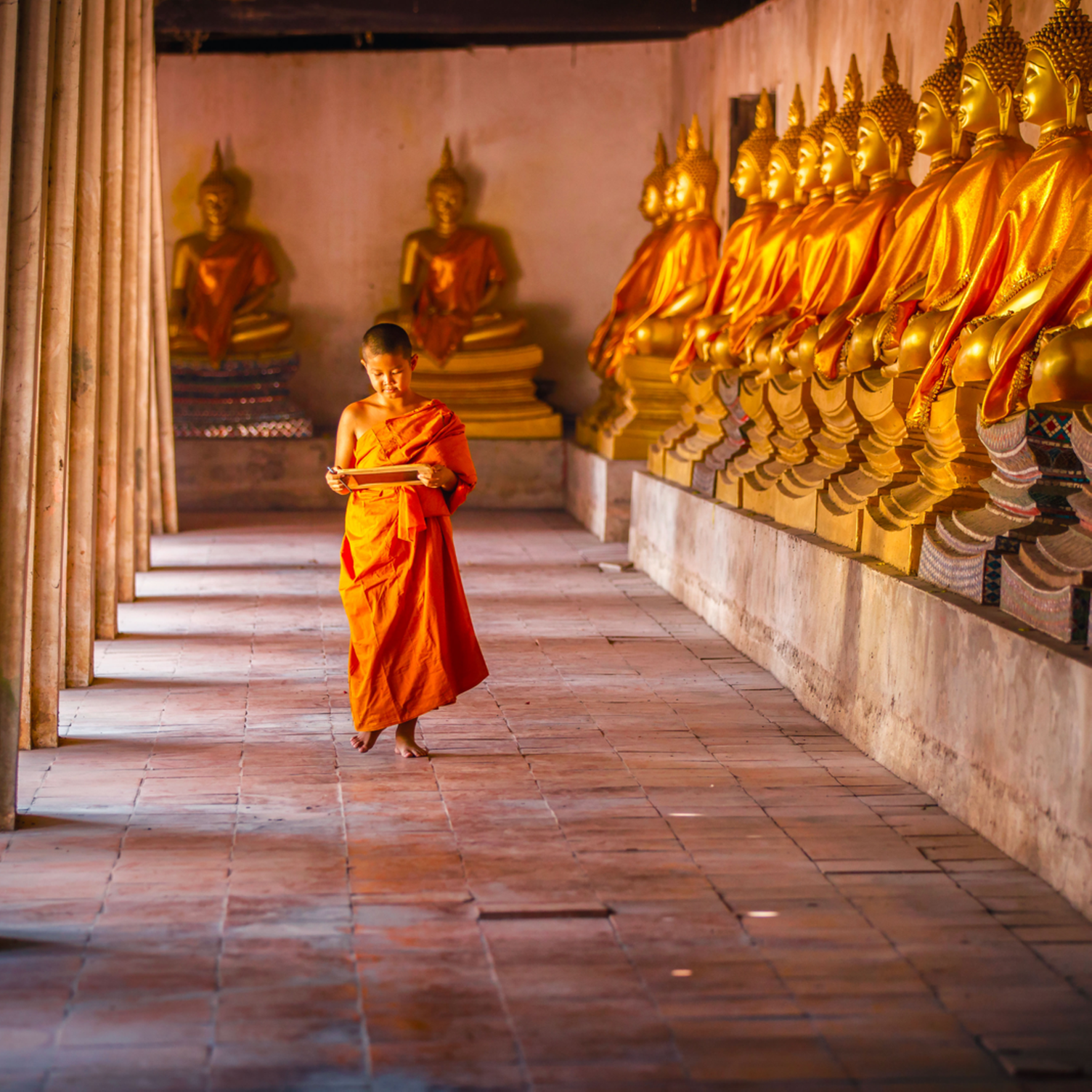 Jeune moine thaï marchant dans une galerie ornée de bouddhas dorés