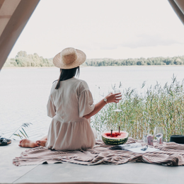 Jeune femme de dos pique-niquant devant une tente face à un lac