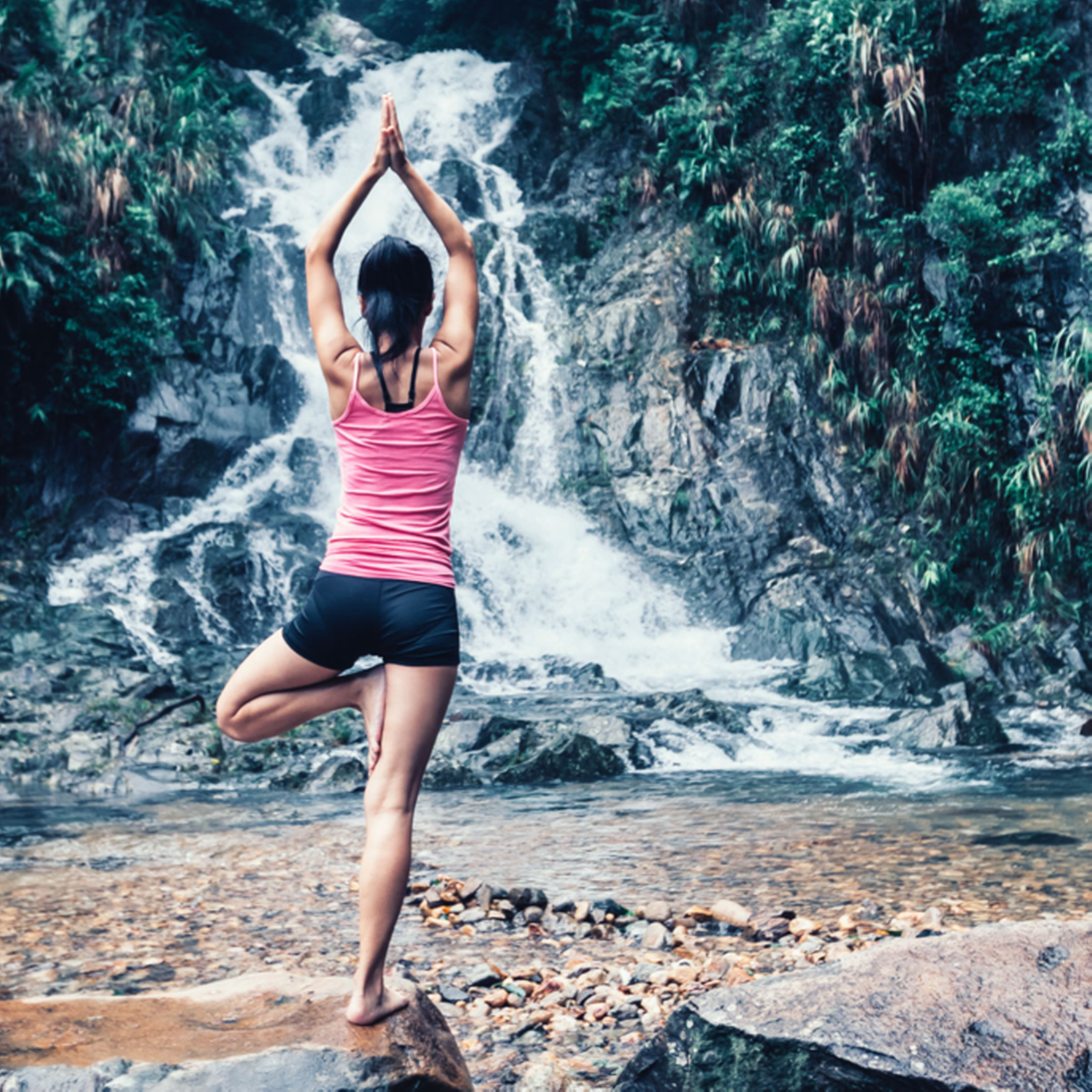 Junge Frau macht Yoga vor einem Wasserfall