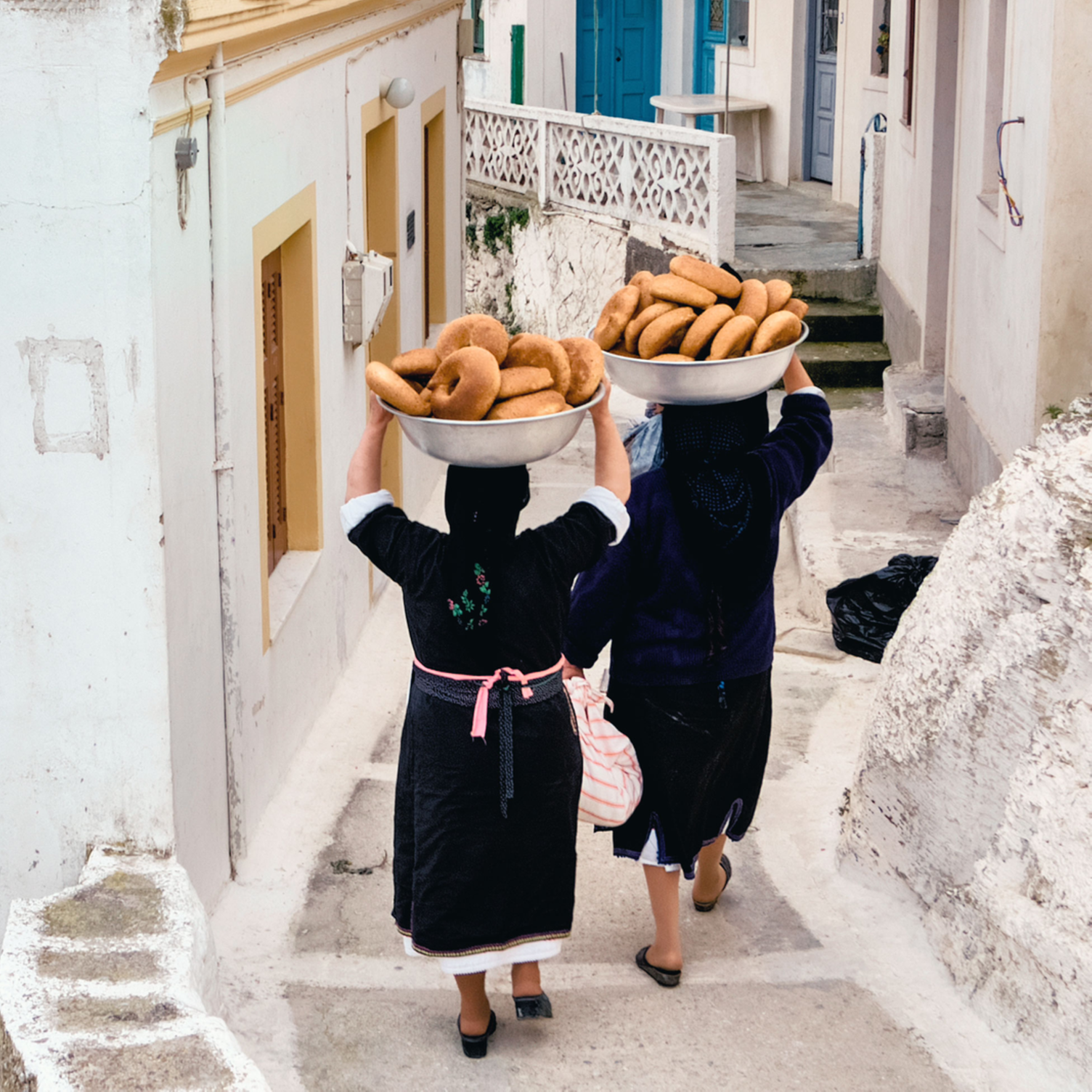 Femmes de dos marchant en portant les pains de Pâques dans une ruelle d'un village grec