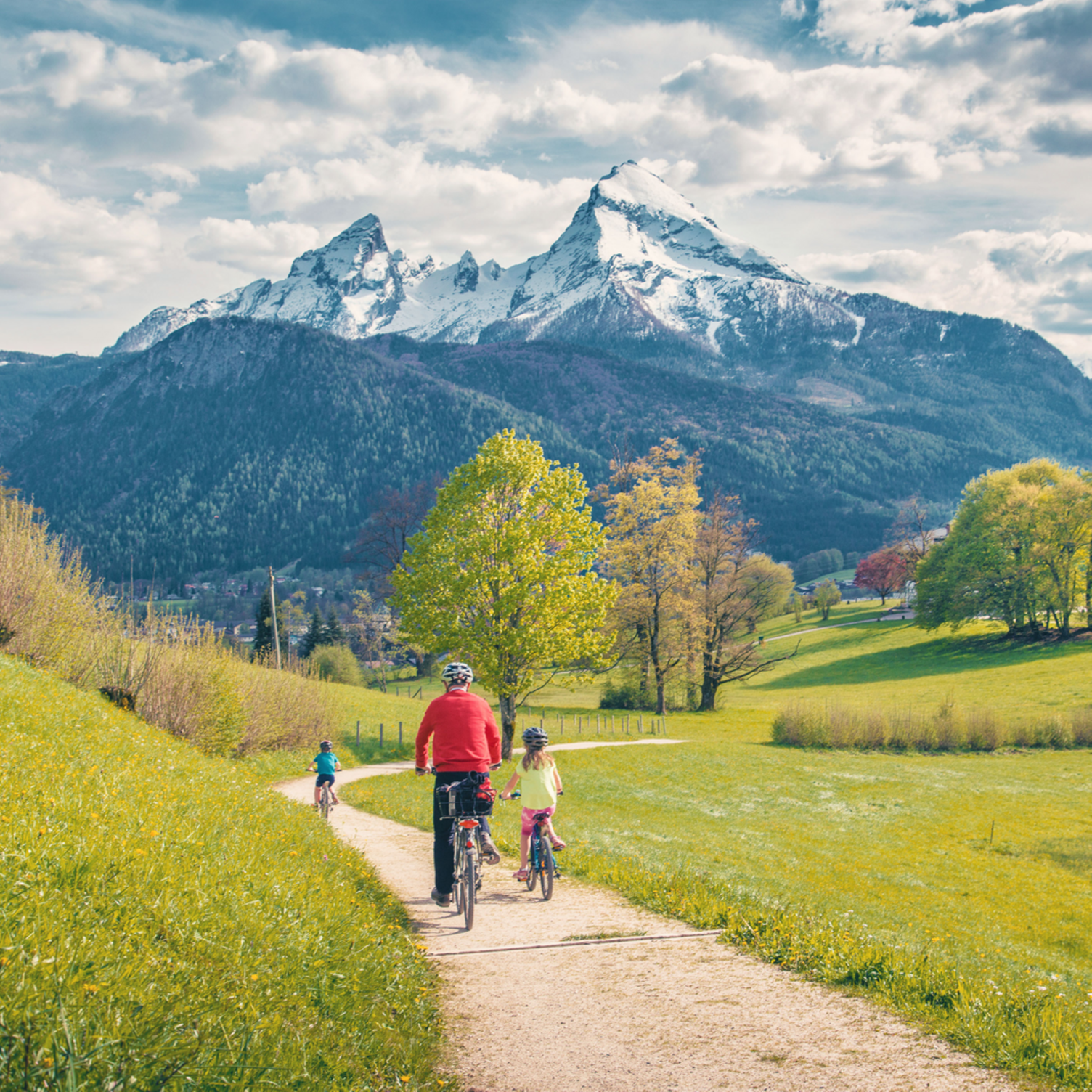 Un adulte et 2 enfants à vélo dans une vallée au pied des montagnes