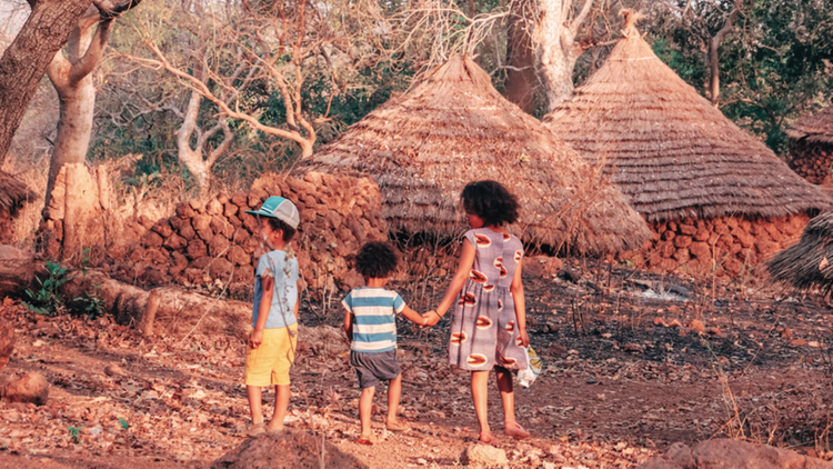 3 enfants se promenant dans un village de cases au Sénégal