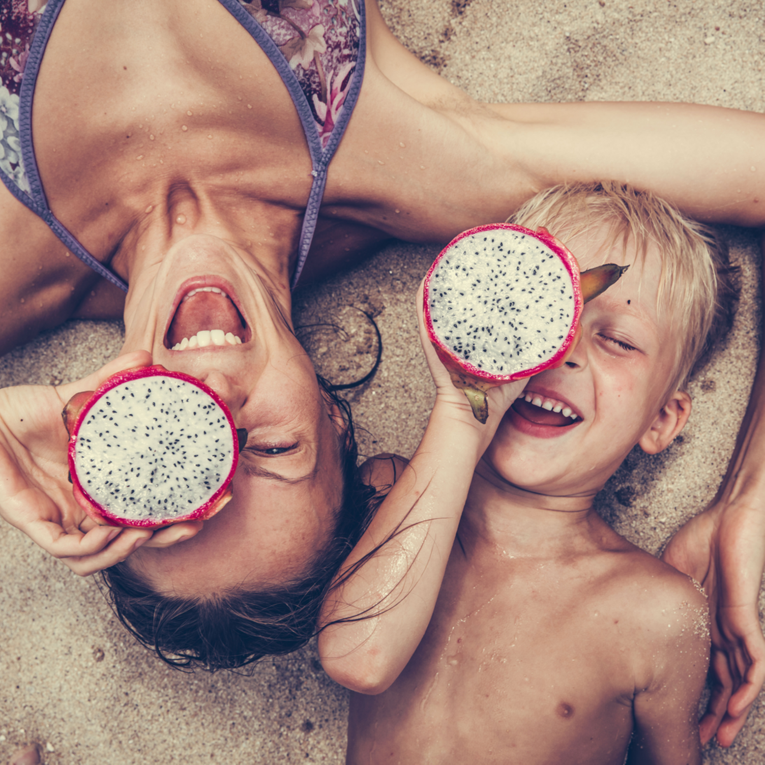 Ein Kind und seine Mutter liegen im Sand und spielen mit Drachenfrüchten