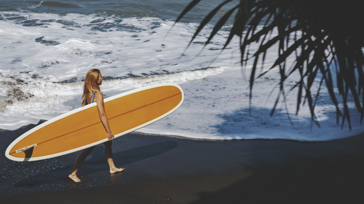 Jeune femme marchant avec un surf sous le bras sur la plage de Balian Beach à Bali