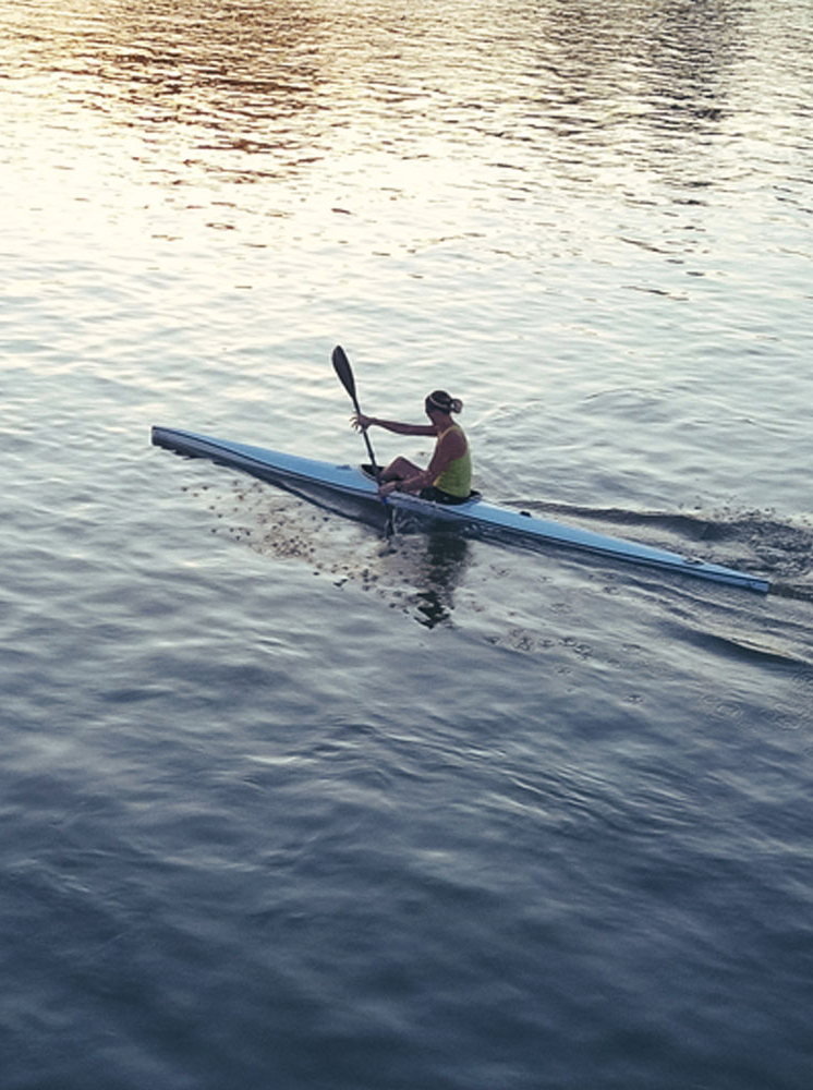 Portrait of active sport woman - She is professional kayaker and practicing on river in summer sunset. Muscular woman rowing and kayaking.