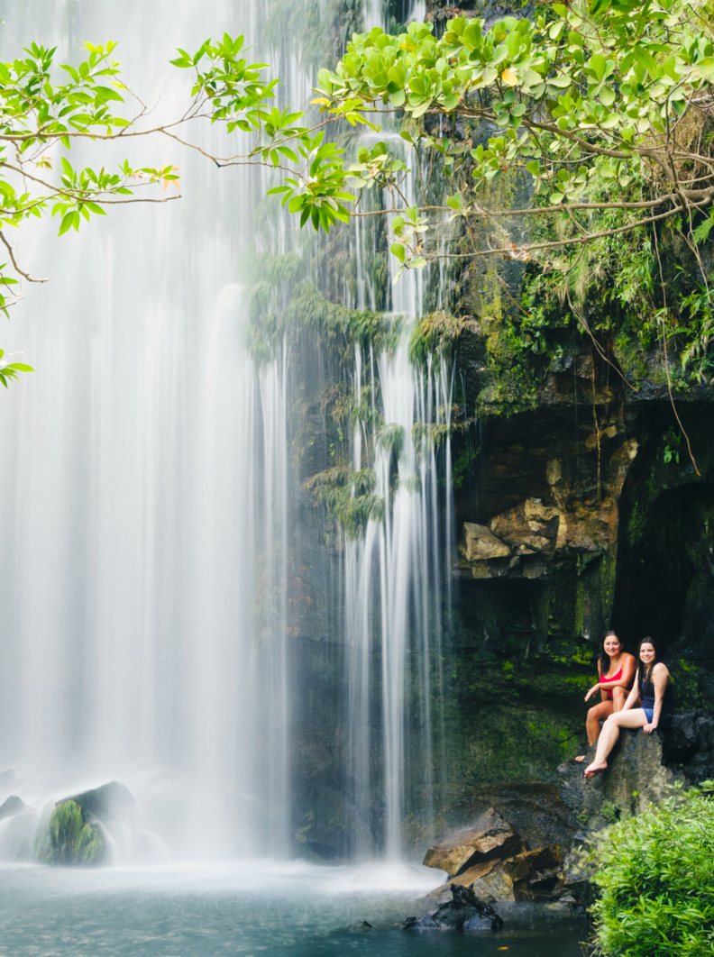 Two women relaxing next to a waterfall. Llanos de Cortes Waterfall in Bagaces, Guanacaste, Costa Rica