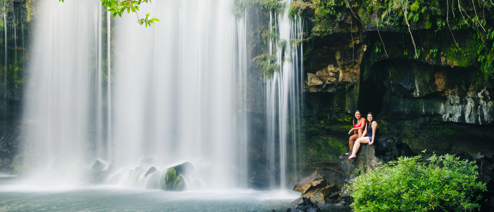 Two women relaxing next to a waterfall. Llanos de Cortes Waterfall in Bagaces, Guanacaste, Costa Rica