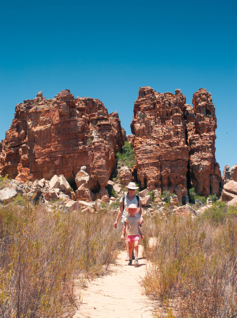 03 A young blond caucasian girl leading her mother walking on a dirt footpath in-between rocks in the Cederberg wilderness area and mountains South Africa