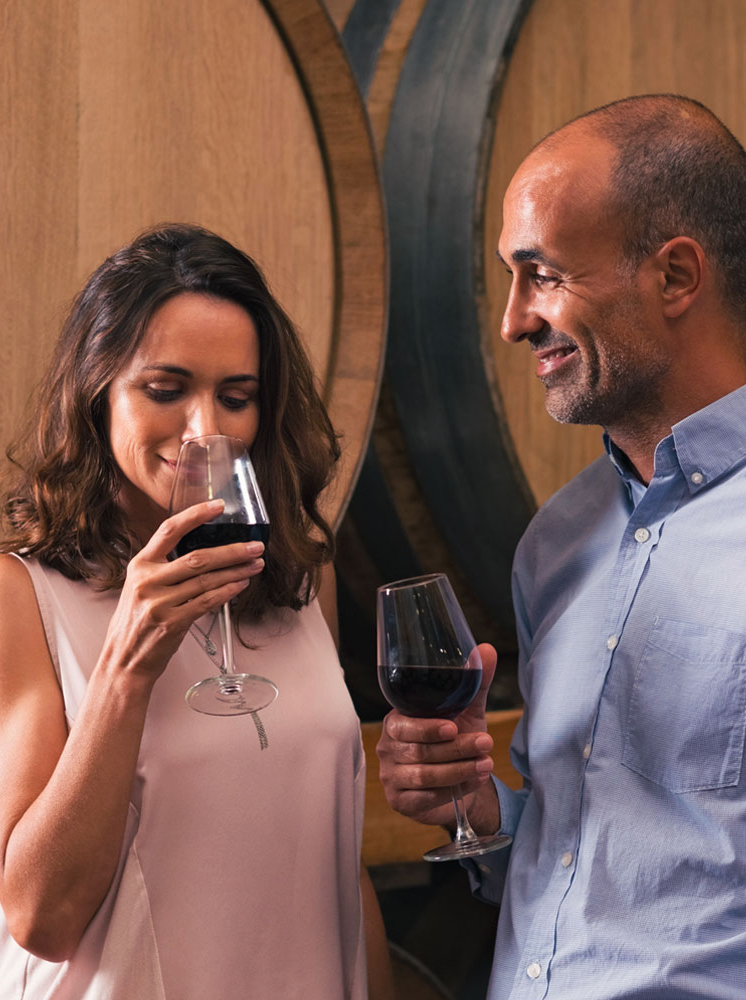 Mature couple tasting a glass of red wine in a traditional cellar surrounded by wooden barrels. Happy mature woman smelling a glass of red wine. Loving couple tasting wines in winery cellar."r