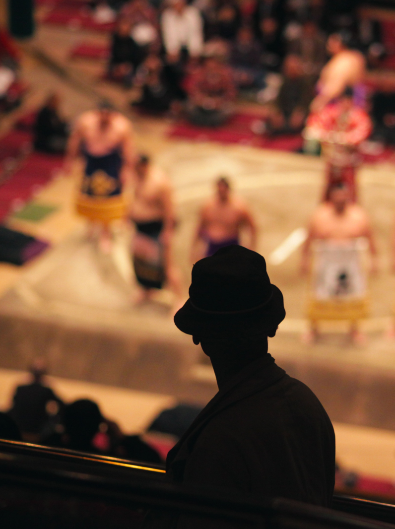 Silhouette of an elderly man watching sumo wrestlers standing in a ceremonial ring