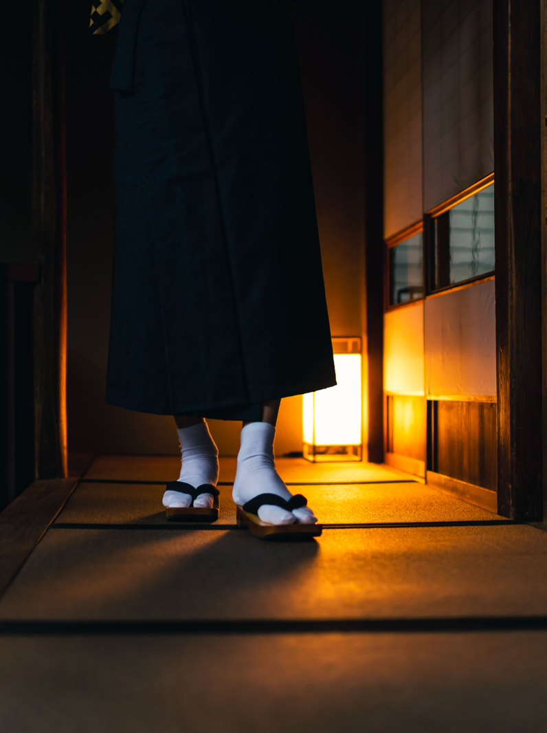 Traditional japanese house or ryokan with man in kimono walking closeup of legs with geta tabi shoes and socks by shoji sliding paper doors and tatami mat floor