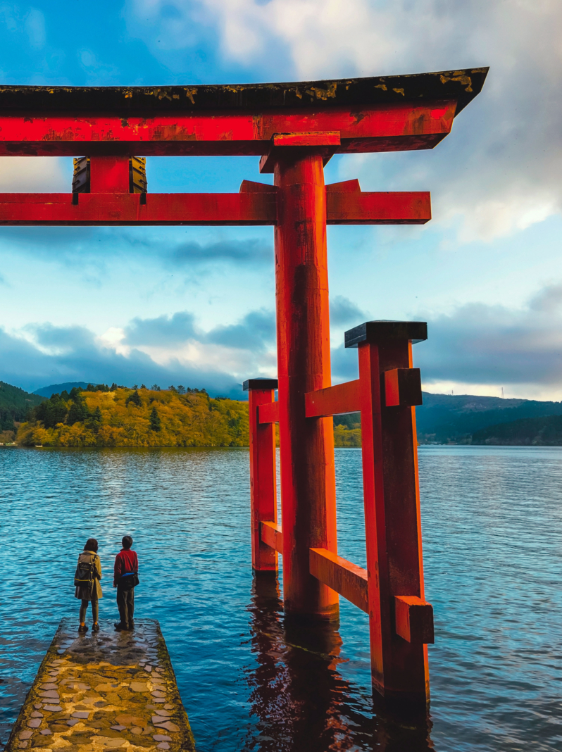 Japanese couple at red Torii gate of Hakone shrine located on lake Ashi, Japan. Gateways entrance to Shinto shrines and famous tourist landmark