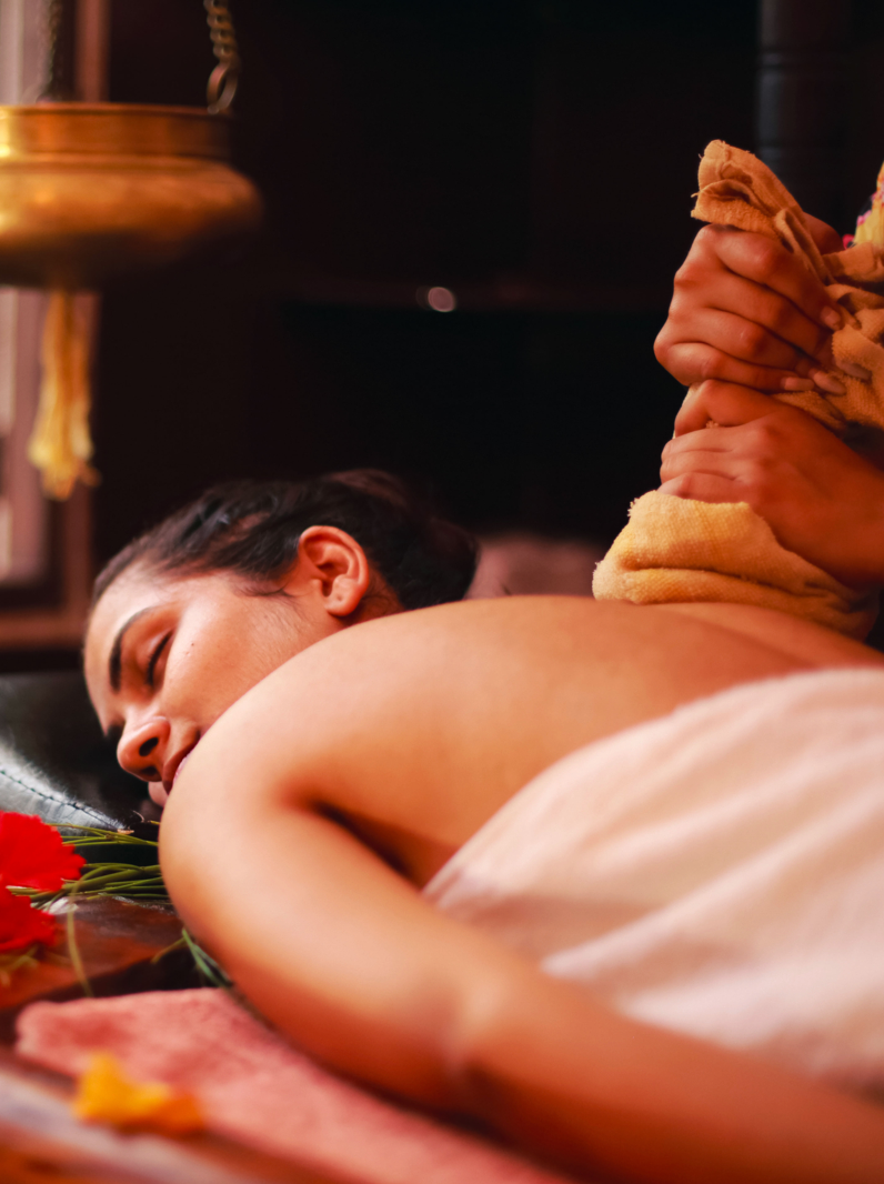 Female therapist treating a young lady in an ayurvedic spa following Indian traditional method