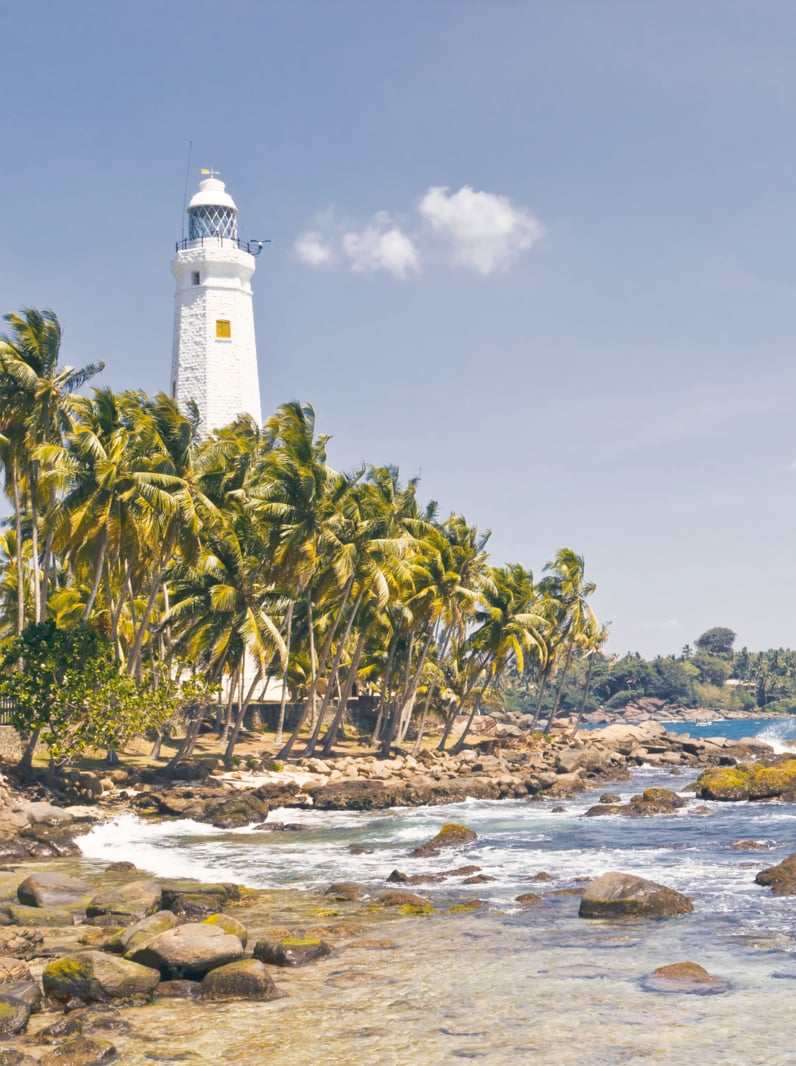 Beautiful tropical landscape with white Dondra Head Lighthouse and palms. Southern point of Sri Lanka coastline, Ceylon