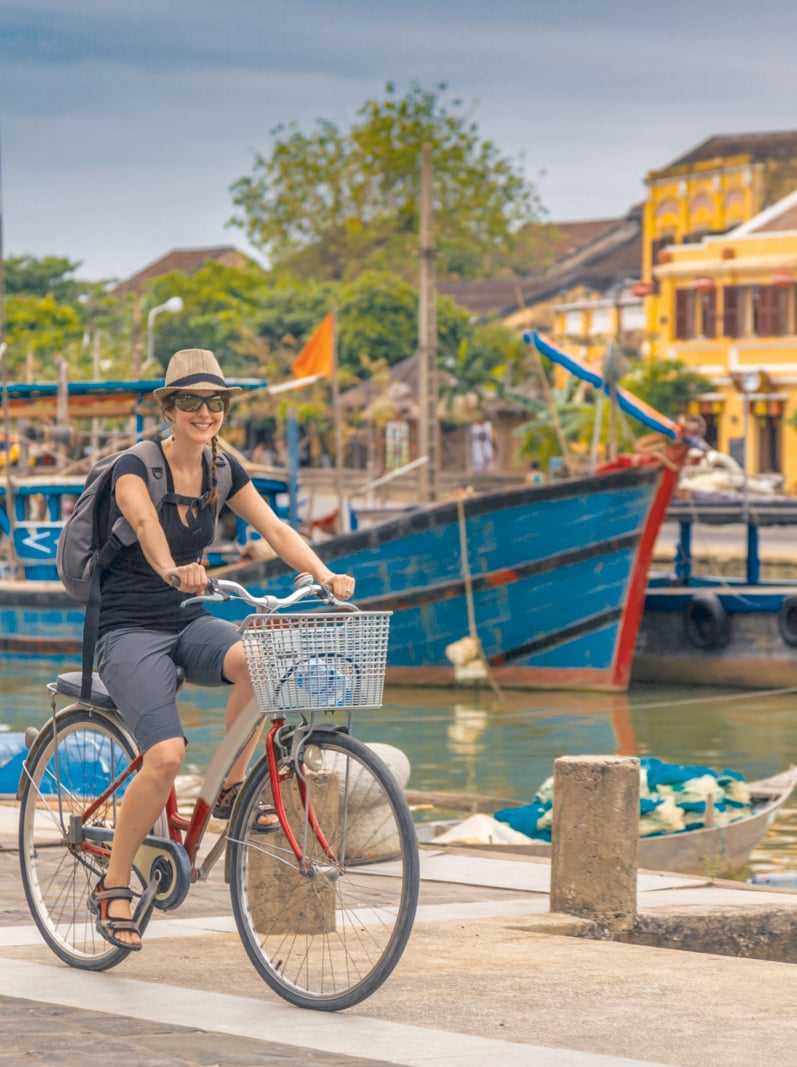 Woman Tourist Cycling in Hoi An City, Vietnam. She is happy and smiling and the coloured buildings of the city are in the background