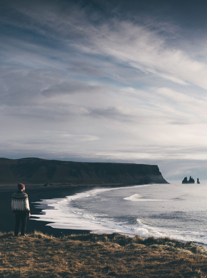 Young Caucasian man in Icelandic sweater looking at the rocks in the sea in Iceland
