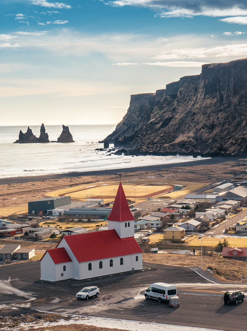 The village of Vik in South Iceland. In the distance the cliffs of Reynisdrangar. In the foreground the wooden church of Vik in Myrdal