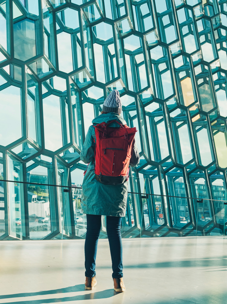A girl with a backpack is standing in front of a glass wall. Modern architecture. Iceland