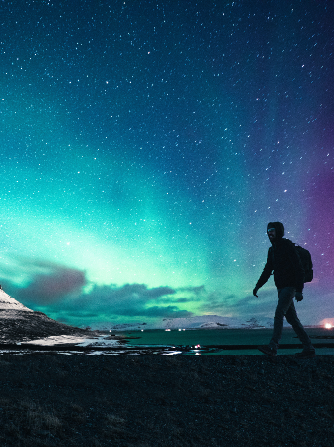 Solo traveler walking in front of an awesome Northern Lights in Mount Kirkjufell Iceland