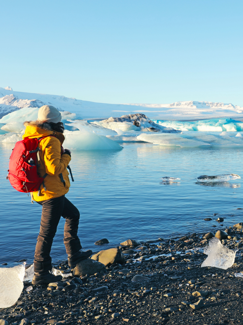 Female traveller is standing at the edge of Jokulsarlon glacial lagoon in Iceland on a beautiful sunny winter day