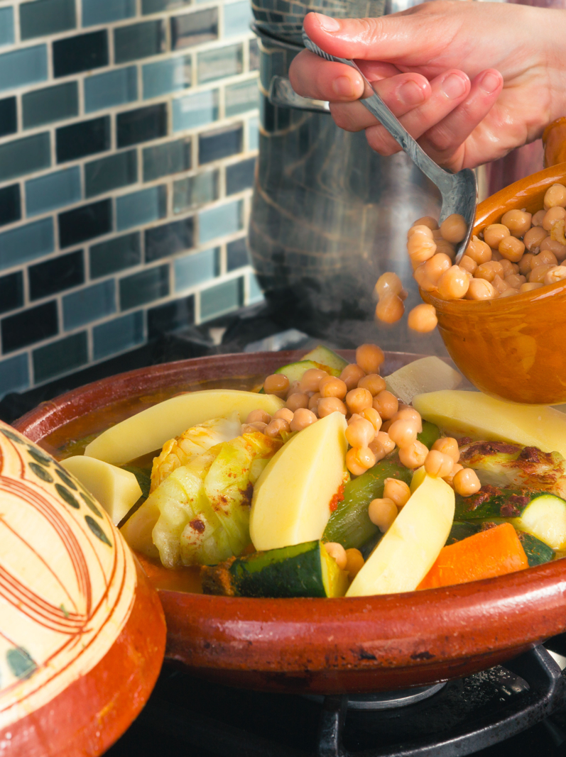 Moroccan woman adding chickpeas to her tajine pot while preparing dinner during ramadan