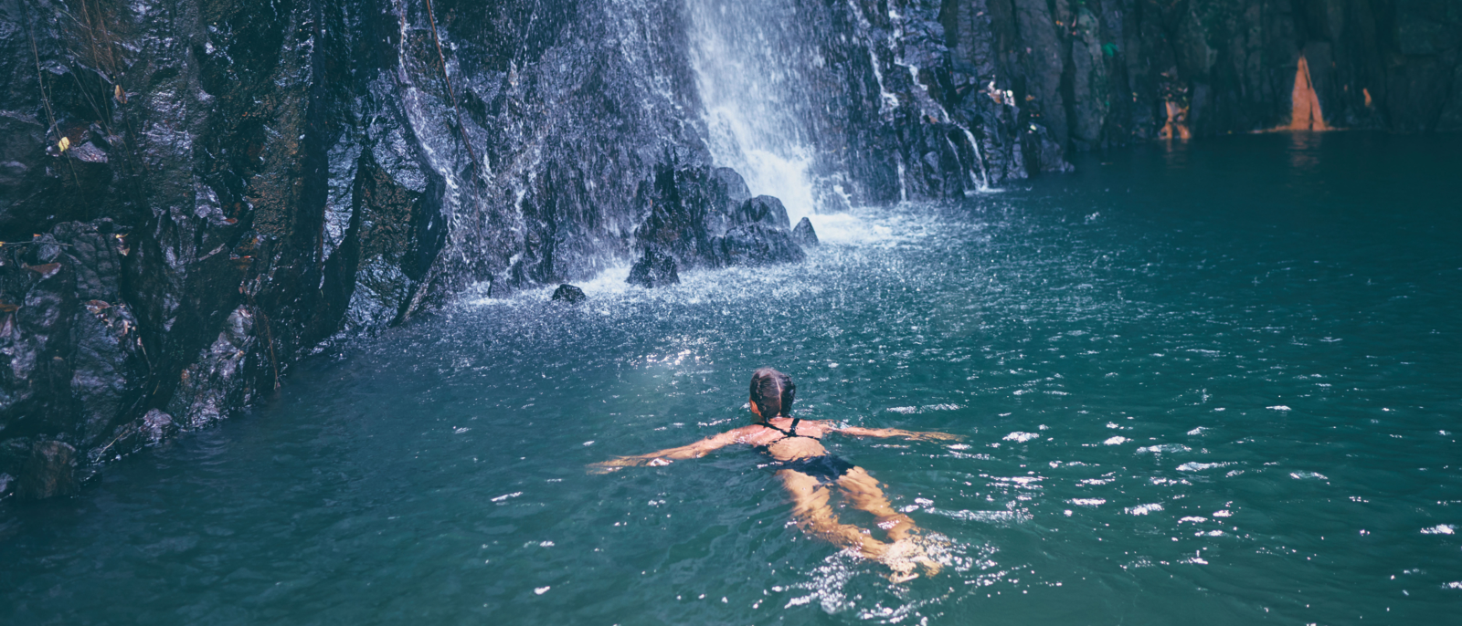 Travel and nature. Young woman swimming in tropical waterfall pool