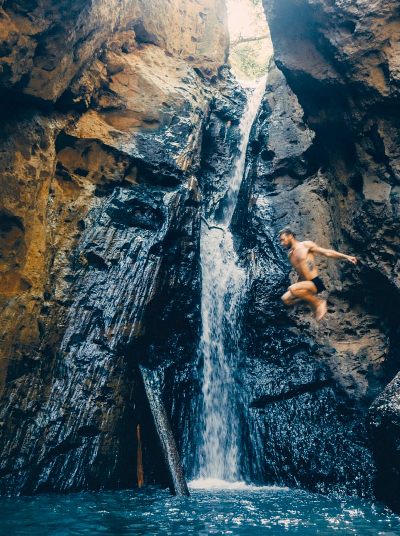 Young Caucasian man jumping from rock into the tropical waterfall in Thailand
