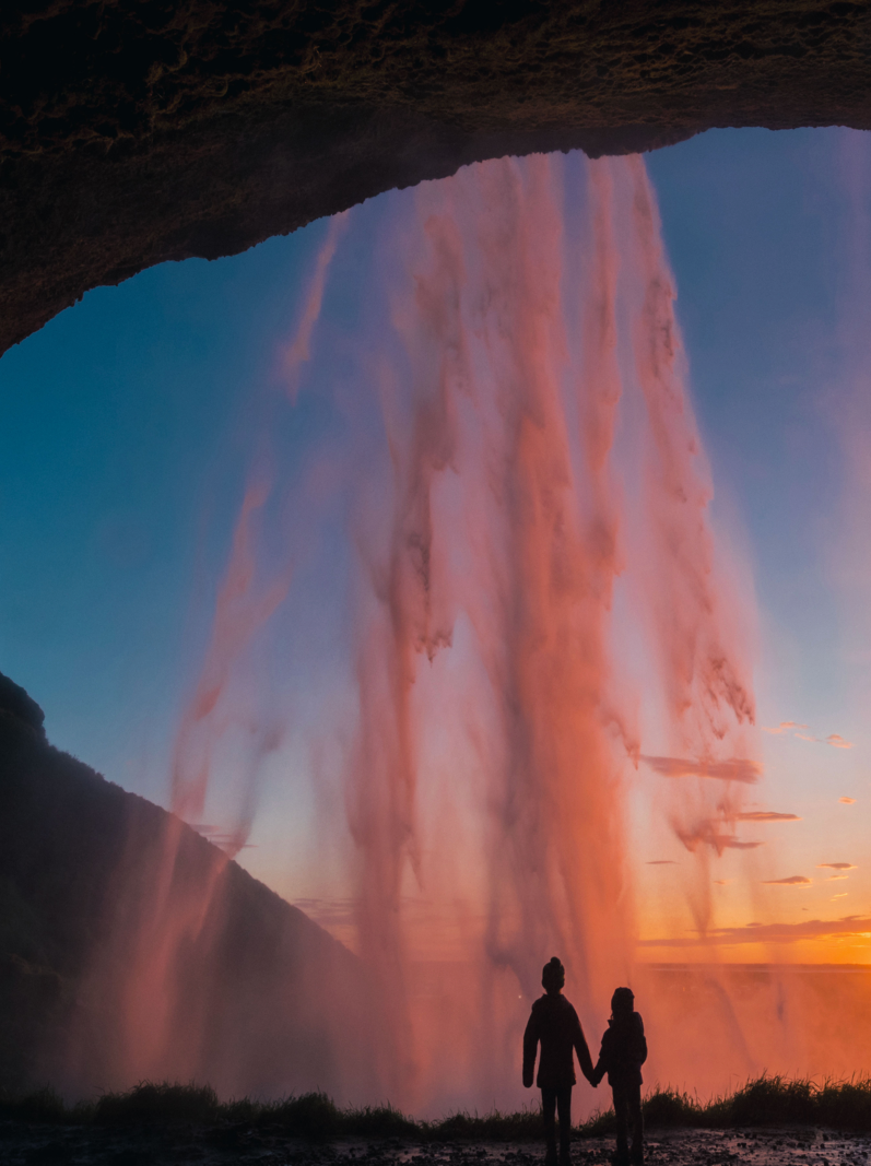 Sisters holding hands behind Seljalandsfoss waterfall