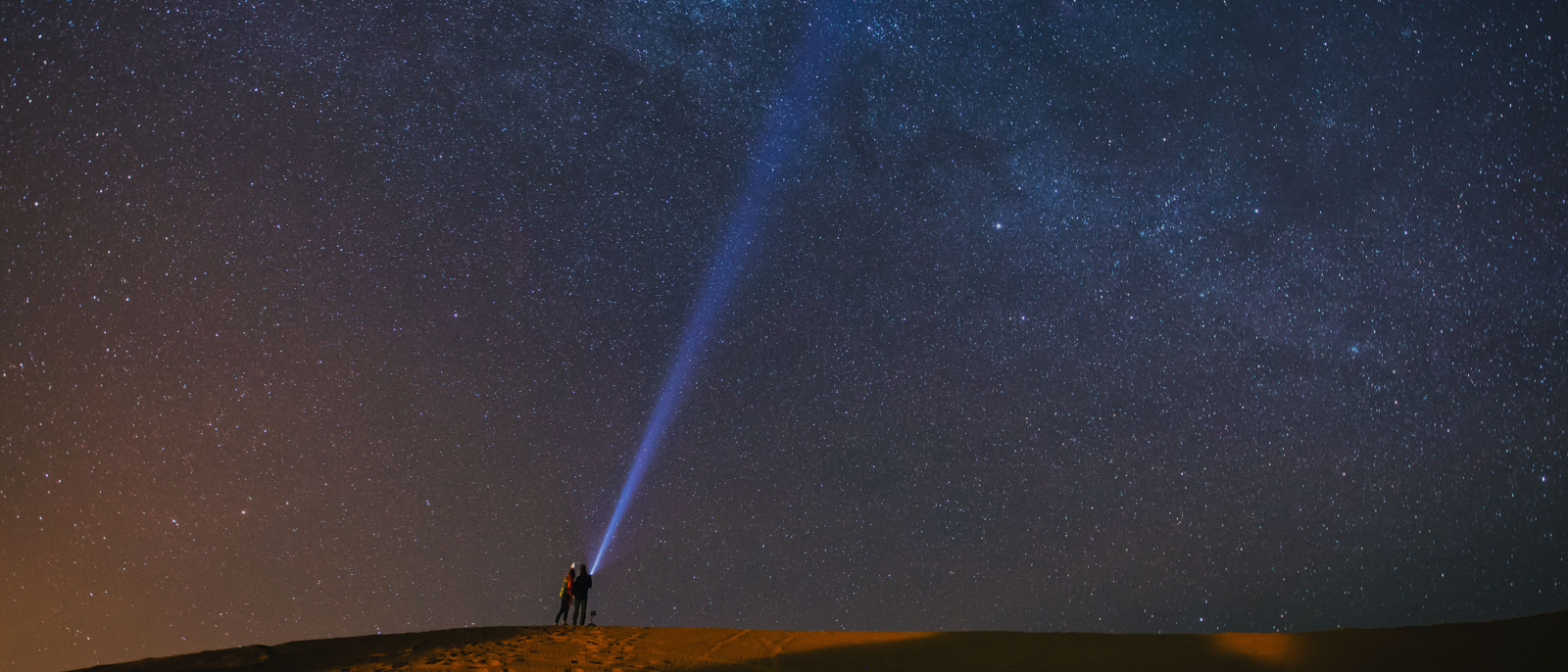 Couple in love playing with flashlight in Desert Sahara with milky way in background, sky full of stars. Morocco