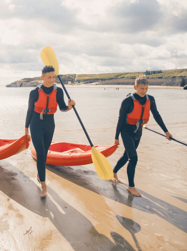 Teenage boys Leaving the sea with their Oars and their kayaks after having fun and racing each other in the sea