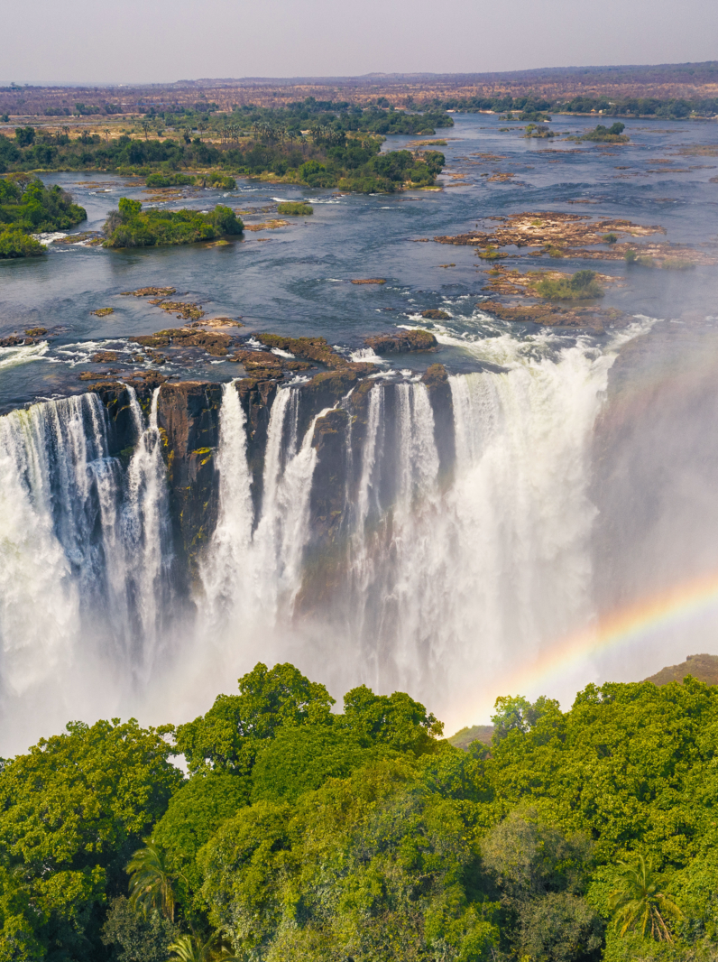 Aerial few of the world famous Victoria Falls with a large rainbow over the falls. This is right at the border between Zambia and Zimbabwe in Southern Africa. The mighty Victoria Falls at Zambezi river are one of the most visited touristic places in Africa.