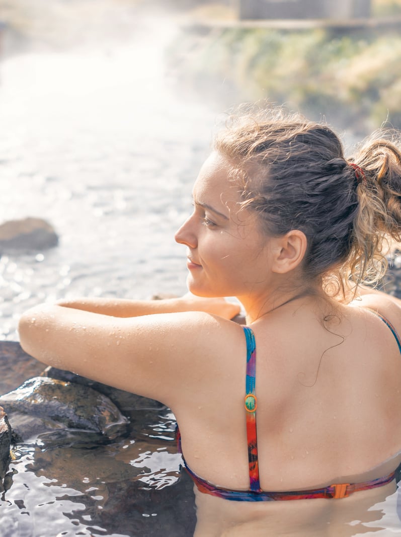 Back of young woman swimming bathing in Hveragerdi Hot Springs on trail in Reykjadalur, profile side in south Iceland, golden circle, rocks and river steam