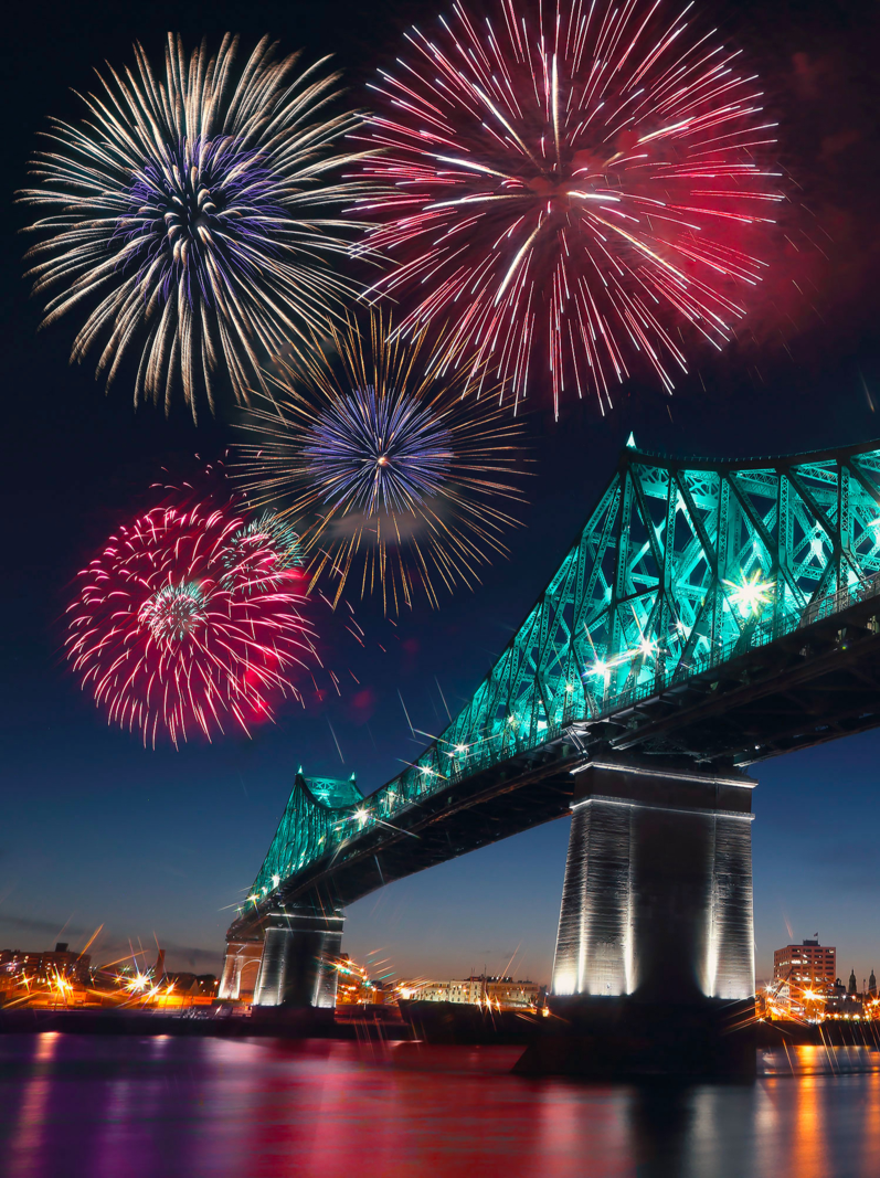 Des feux d'artifice colorés explosent sur le pont, reflétant dans l'eau. Le 375e anniversaire de Montréal. Pont lumineux et interactif Jacques Cartier