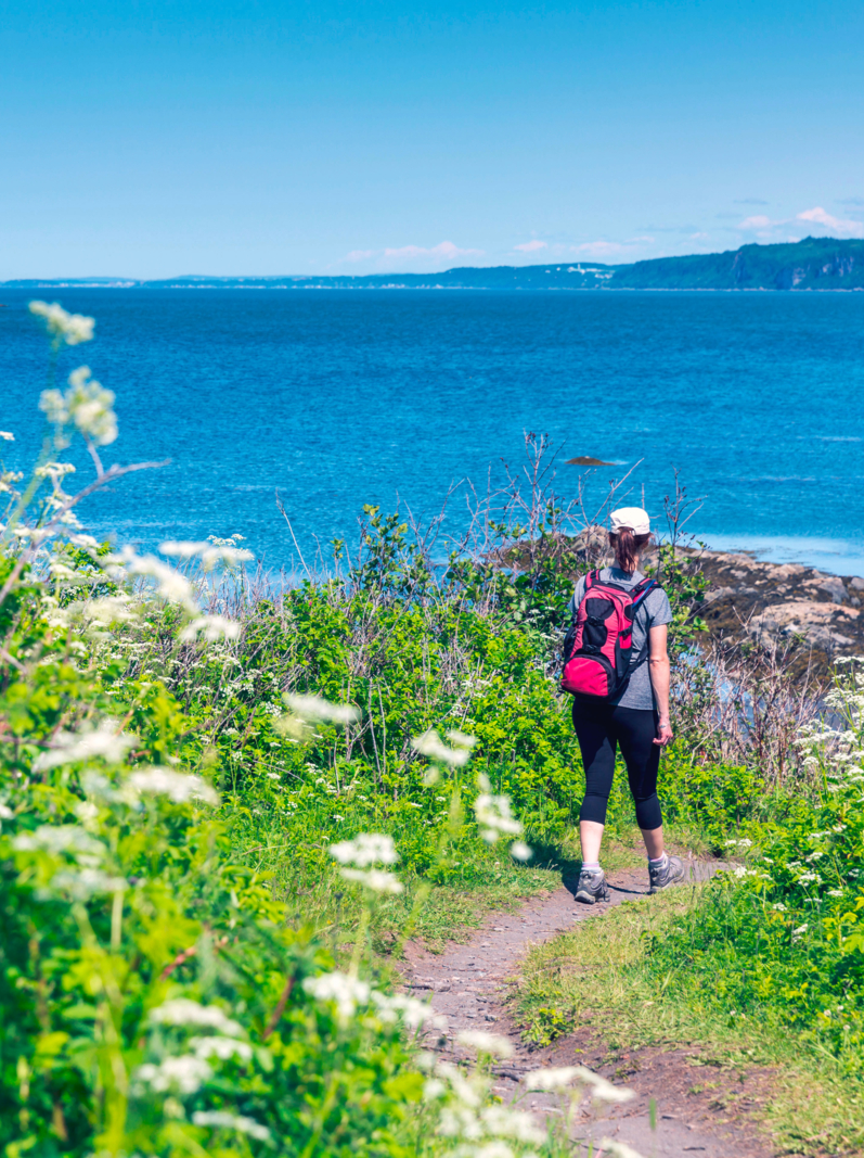Woman hiker walking with a backpack on a trail along the St-Lawrence River, Quebec, Canada. Taken at the Bic National Park.