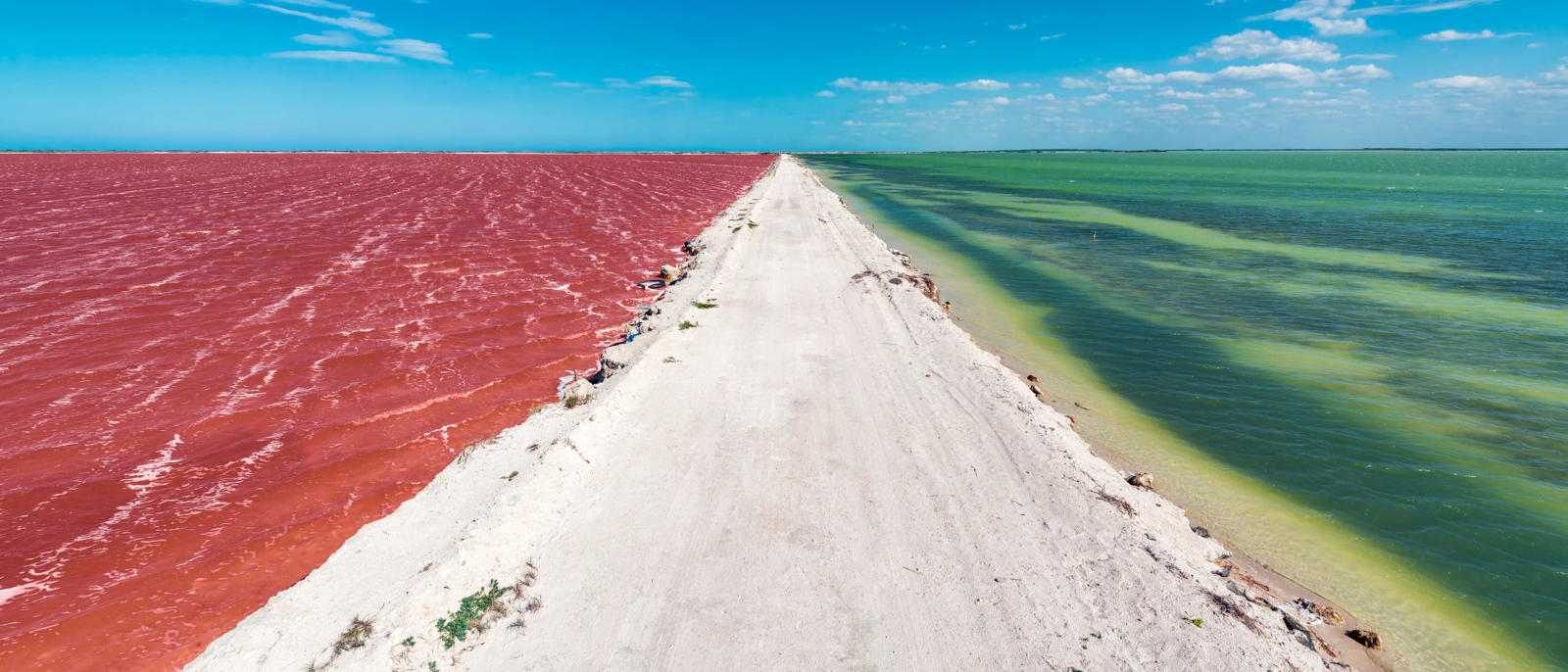 Une route irrégulière avec de l'eau rouge d'un côté et de l'eau verte de l'autre avec un beau ciel bleu près de la ville de Las Coloradas près de Rio Lagartos, Mexique