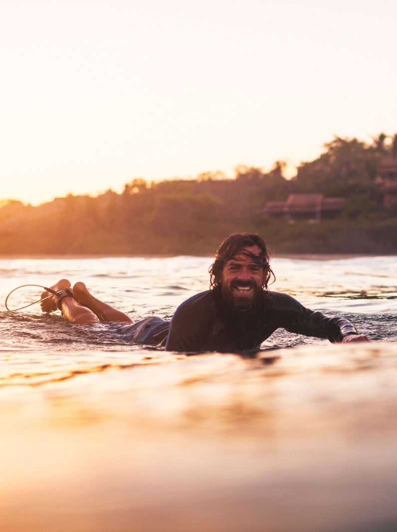 surfer paddling in ocean wave at sunrise