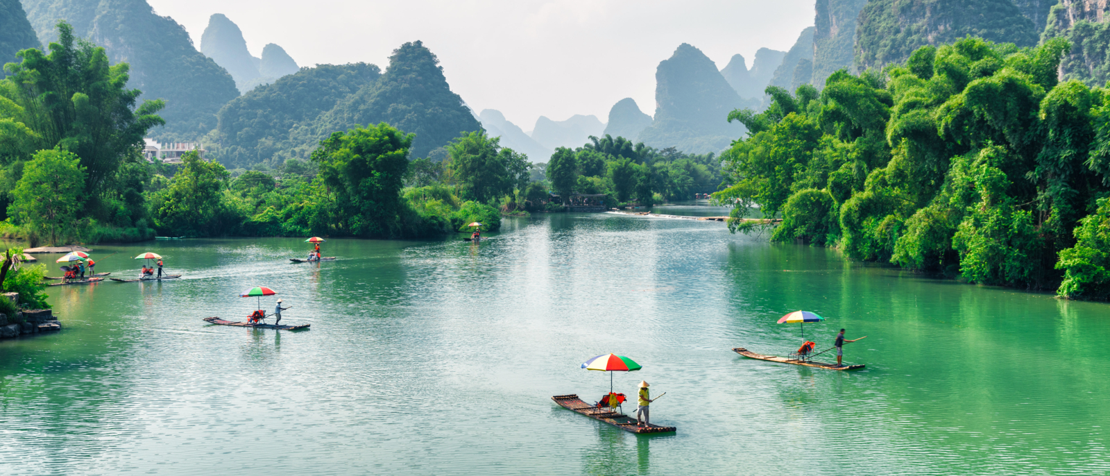 Scenic view of small tourist bamboo rafts sailing along the Yulong River among green woods and karst mountains at Yangshuo County of Guilin, China