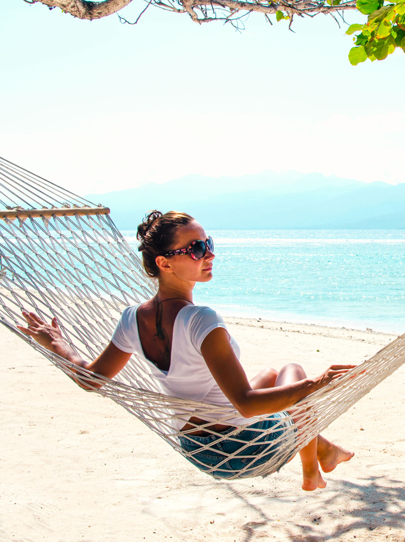 Girl relaxing in hammock on the beach near blue ocean