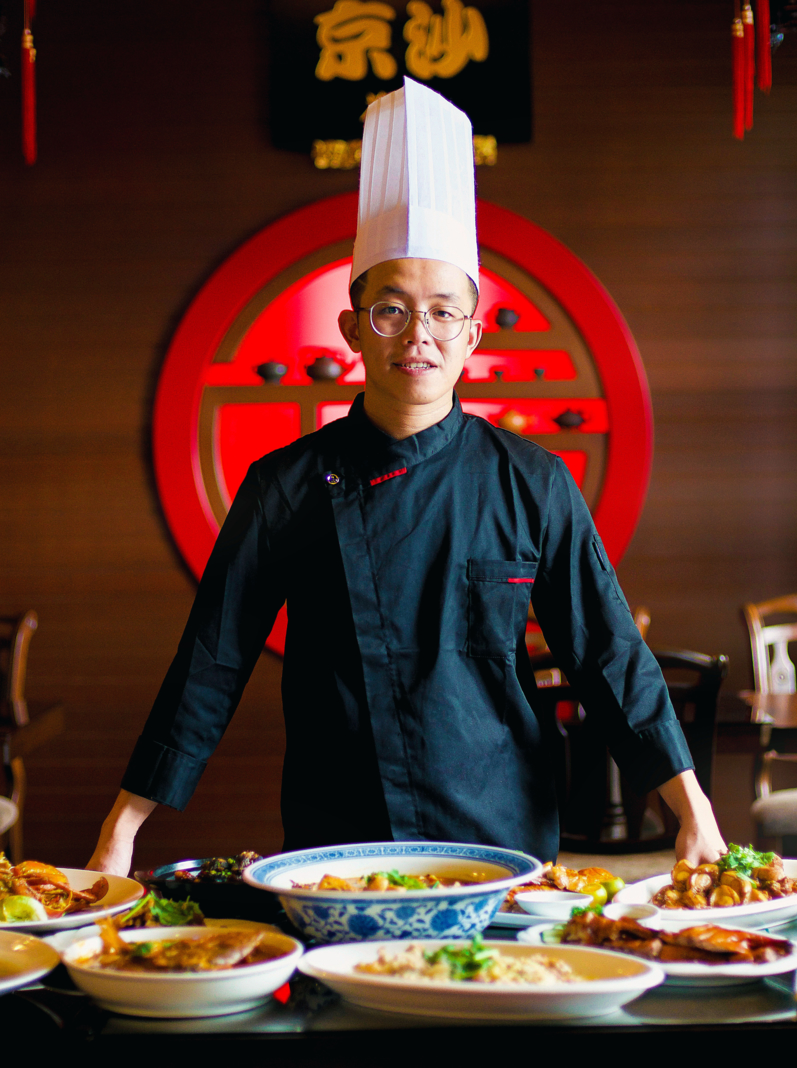 Young Asian chef displaying his special traditional gourmet on the table in an Oriental restaurant setting. Dinner for family. Chinese New Year ambiance