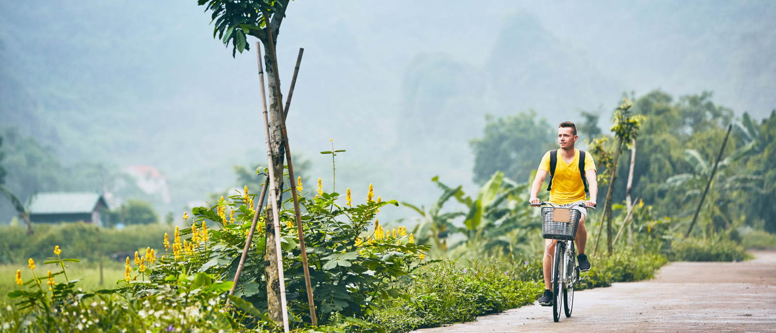 Trip by bike. Man with backpack bicycling on road against karst formation in Ninh Binh province, Vietnam