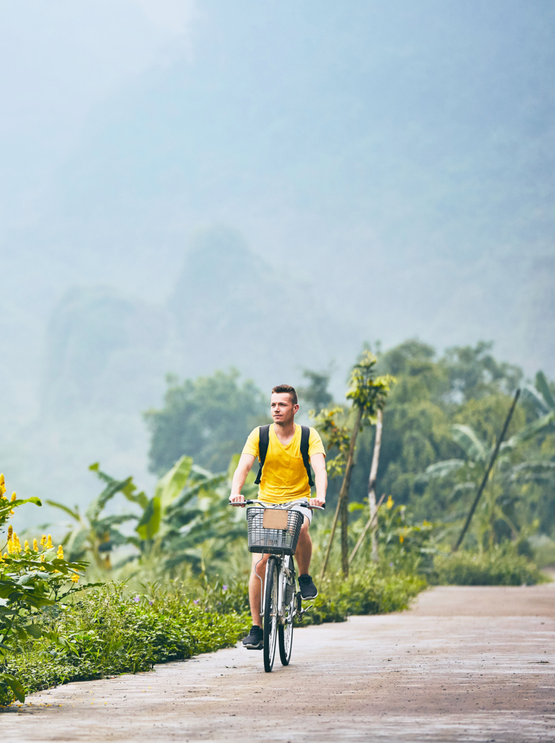 Trip by bike. Man with backpack bicycling on road against karst formation in Ninh Binh province, Vietnam
