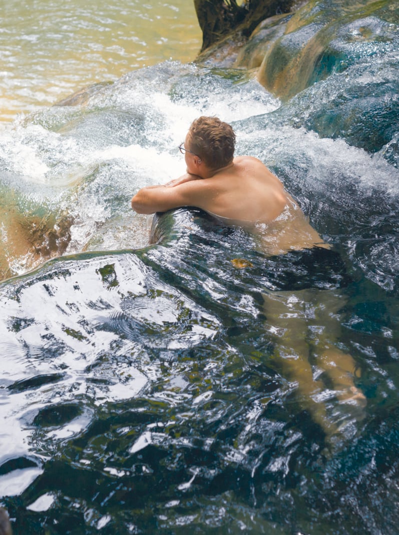 Young man tourist taking healthy bath in Krabi hot springs waterfall in southern Thailand. Tourism in beautiful south east Asia.
