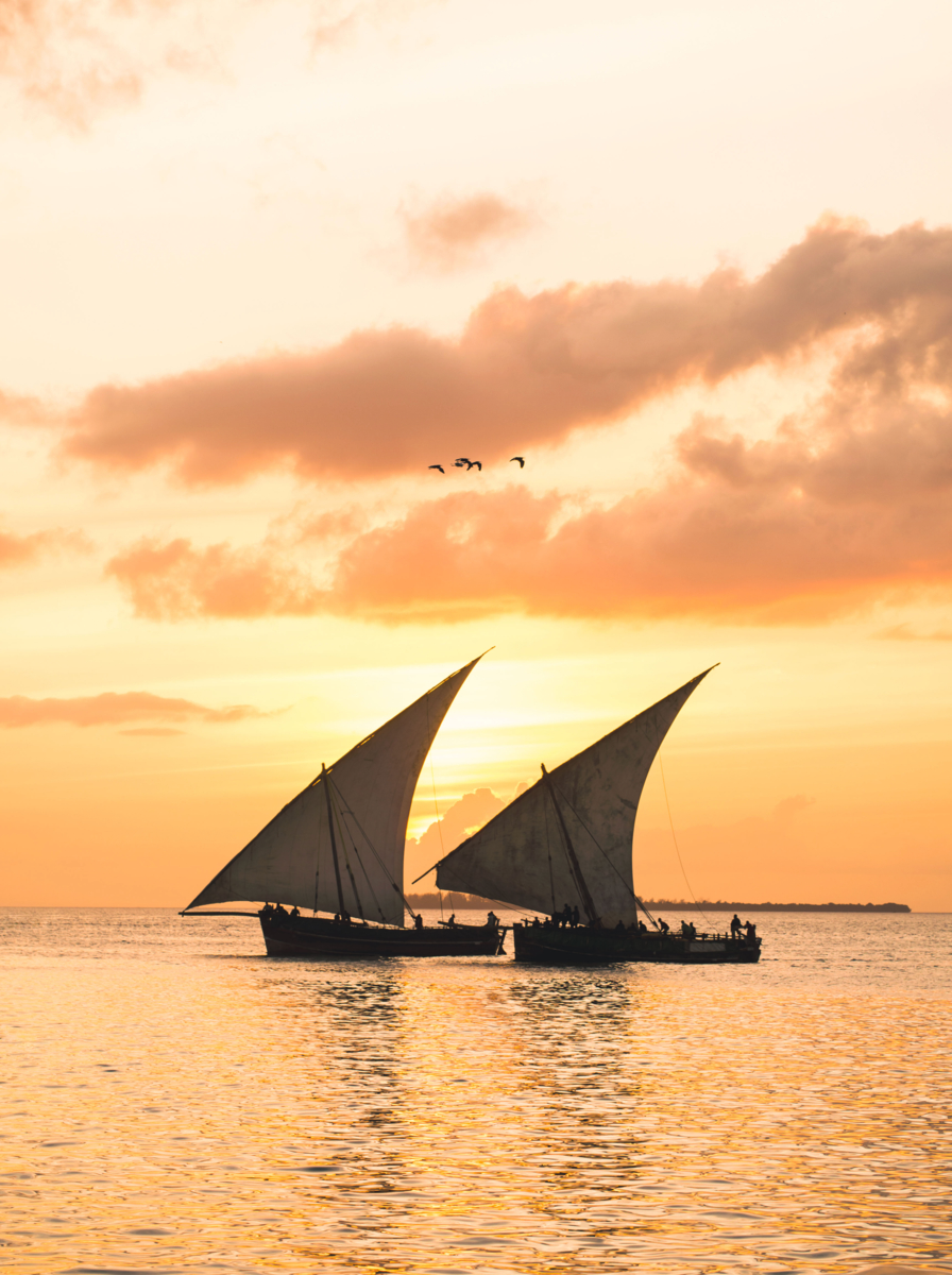 Colorful vertical photo of two traditional Tanzanian dhow boats on open sea on Indian Ocean close to Stone Town on Zanzibar island, Tanzania in East Africa, at orange sunset