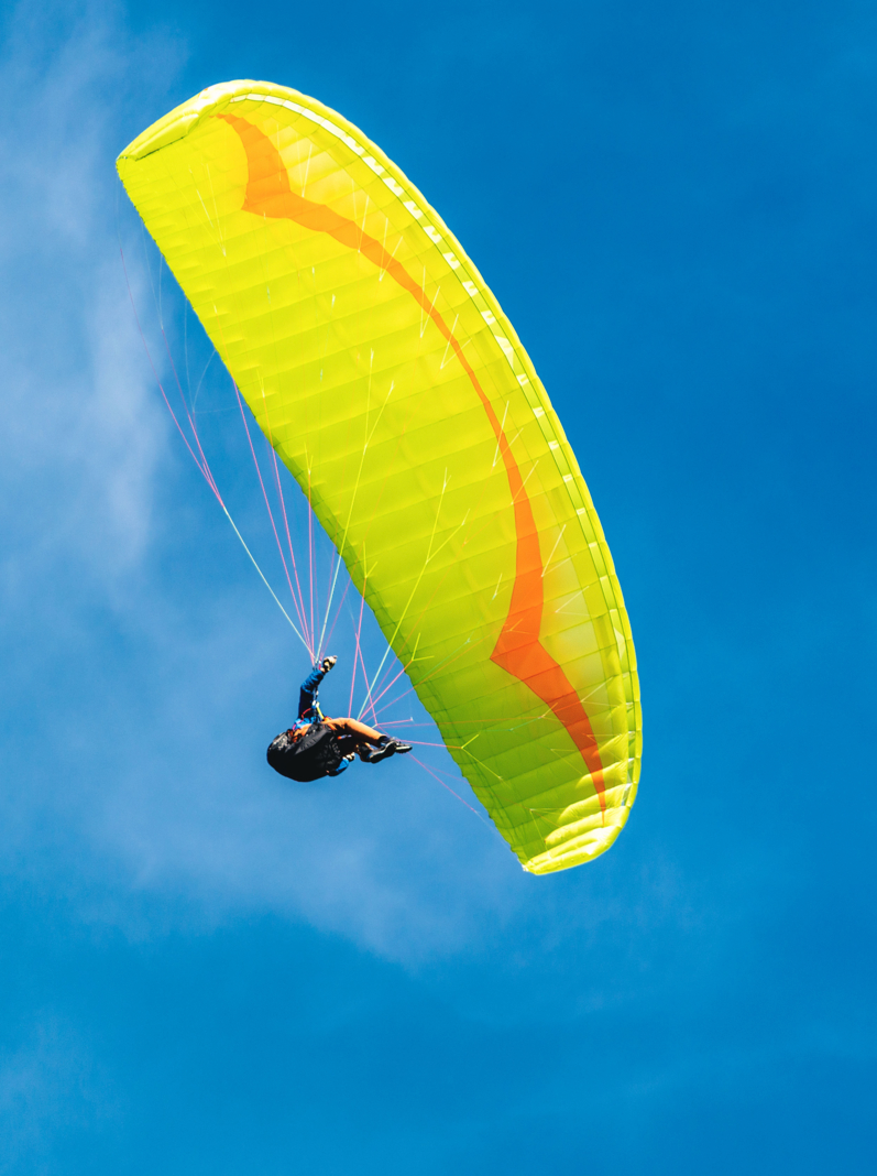 Yellow and orange paragliding on a blue sky with clouds on background