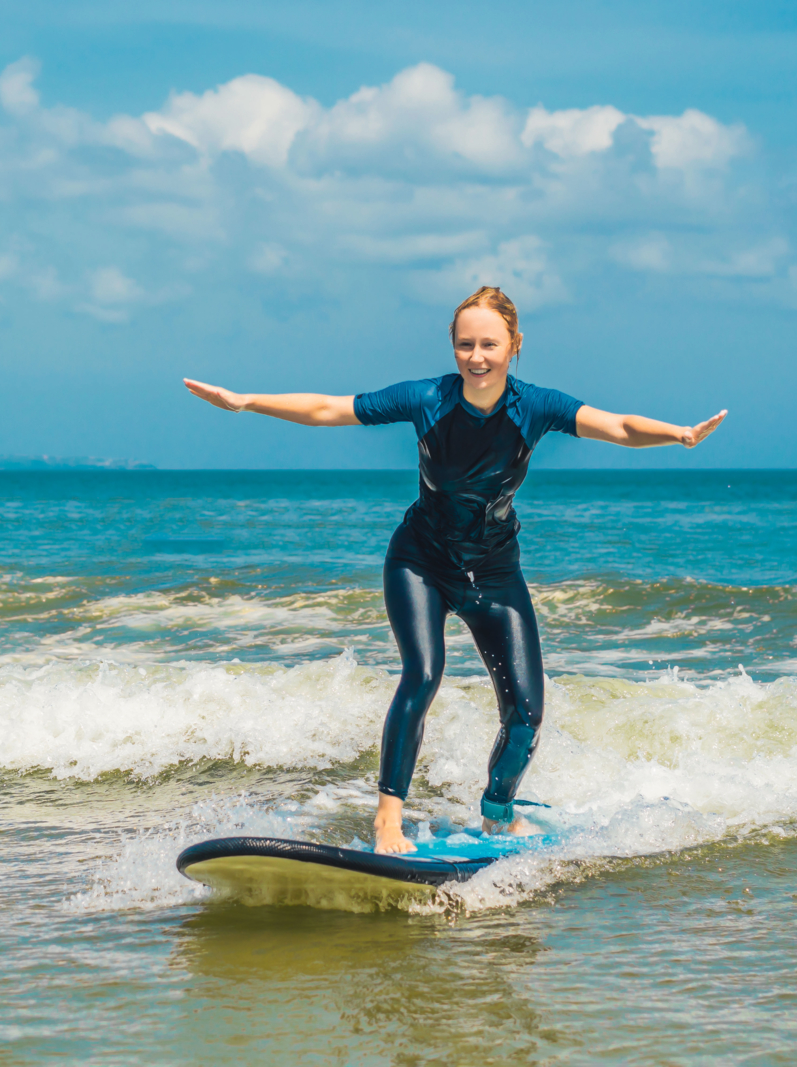 Joyful young woman beginner surfer with blue surf has fun on small sea waves. Active family lifestyle, people outdoor water sport lesson and swimming activity on surf camp summer vacation