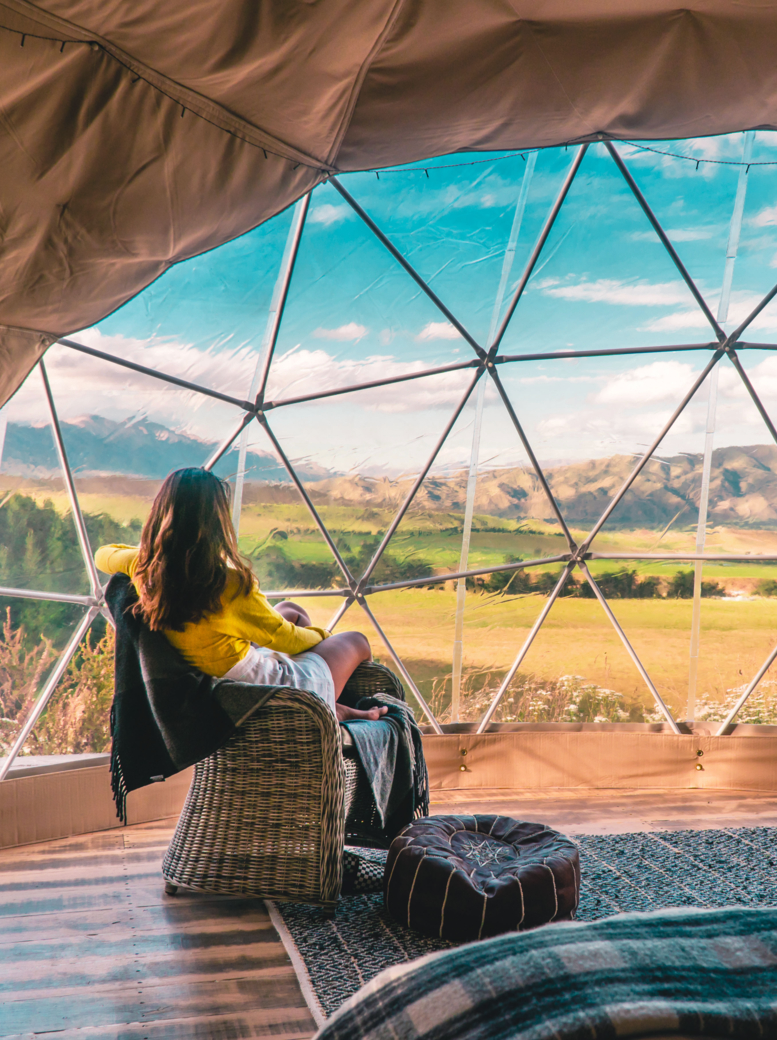 Femme regardant la nature depuis des tentes de geo dome. Vert, bleu, arrière-plan orange. Confortable, camping, glamour, vacances, concept de vie de vacances. Cabine extérieure, arrière-plan scénique. Nouvelle-Zélande