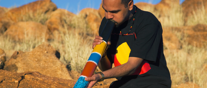 An Aboriginal man playing a colouful didgeridoo in the outback of Australia