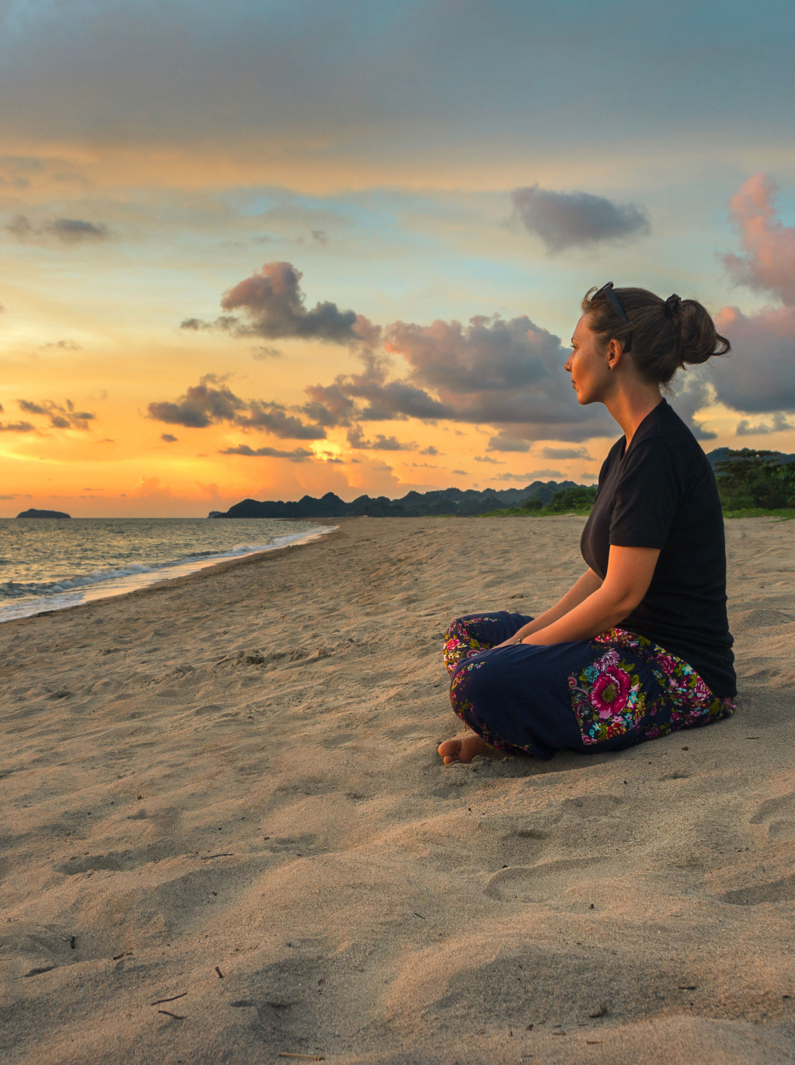 Femme assise sur le sable de la plage et se reposant au coucher du soleil