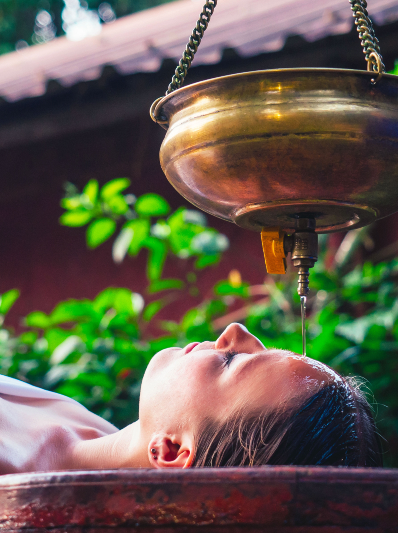 massage ayurveda thérapie alternative.belle femme caucasienne recevant un traitement shirodhara allongée sur une table en bois dans un salon indien