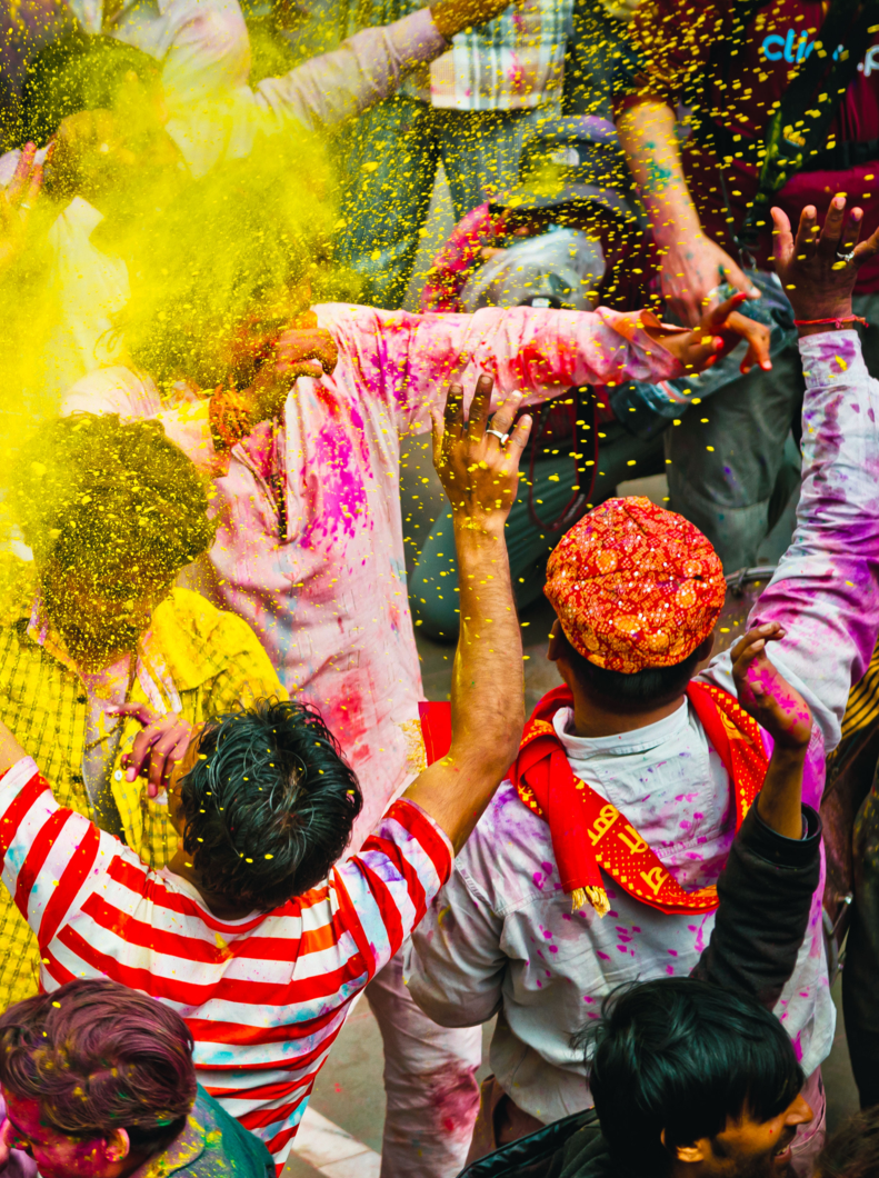 crowd of paint covered villagers celebrate Holi by dancing and throwing colors to each other. Holi is the most celebrated and colorful religious festival in India.
